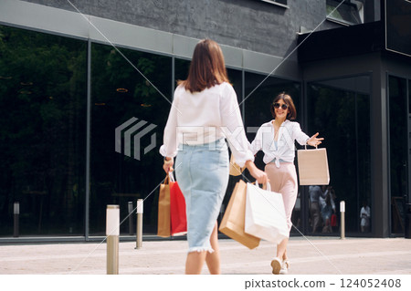Positive buyers. Two female friends have a shopping day. Walking outdoors with bags 124052408