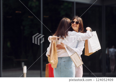 Positive buyers. Two female friends have a shopping day. Walking outdoors with bags 124052409
