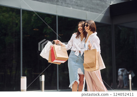 Positive buyers. Two female friends have a shopping day. Walking outdoors with bags Positive buyers. Two female friends have a shopping day. Walking outdoors with bags 124052411