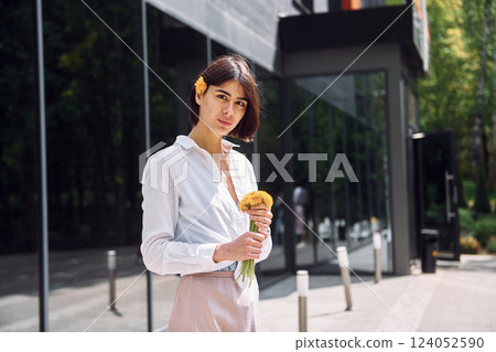 Beautiful brunette is standing outdoors with flowers in her hands Beautiful brunette is standing outdoors with flowers in her hands 124052590