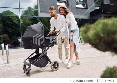 Conception of love. Young parents having a walk with baby carriage outdoors 124052605