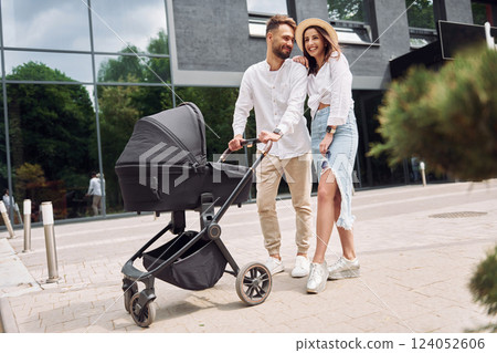 Conception of love. Young parents having a walk with baby carriage outdoors 124052606