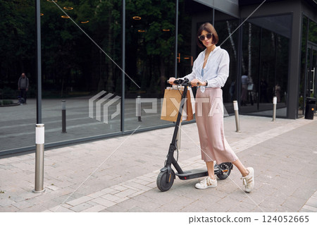 In sunglasses. Beautiful young woman is with her scooter outdoors In sunglasses. Beautiful young woman is with her scooter outdoors 124052665