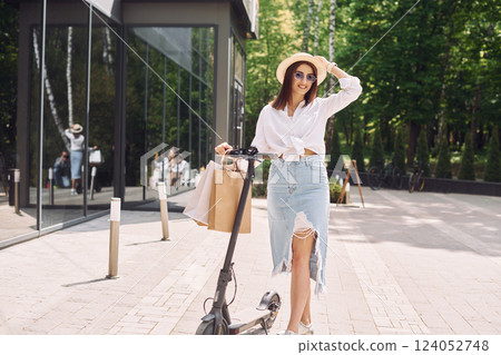 Against modern building. Beautiful young woman is with her scooter outdoors Against modern building. Beautiful young woman is with her scooter outdoors 124052748