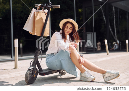 Sitting on the scooter. With shopping bags. Beautiful young woman is outdoors Sitting on the scooter. With shopping bags. Beautiful young woman is outdoors 124052753