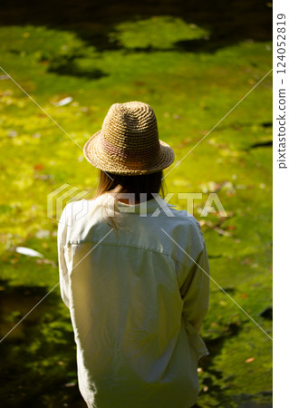 Tourist girl wear natural material clothes and straw hat on a green lake shore in summer forest. Blonde woman on nature. Discover the nature world. Tourist girl wear natural material clothes and straw hat on a green lake shore in summer forest. Blonde woman on nature. Discover the nature world. 124052819