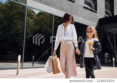 With bags in hand. Young mother with her daughter having a shopping day outdoors together With bags in hand. Young mother with her daughter having a shopping day outdoors together 124052824