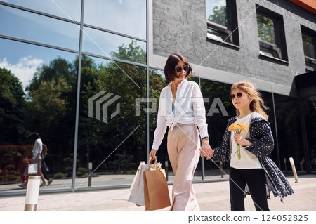 With bags in hand. Young mother with her daughter having a shopping day outdoors together 124052825
