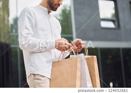 Against building with big windows. Stylish young man have shopping day. Outdoors with bags 124052881