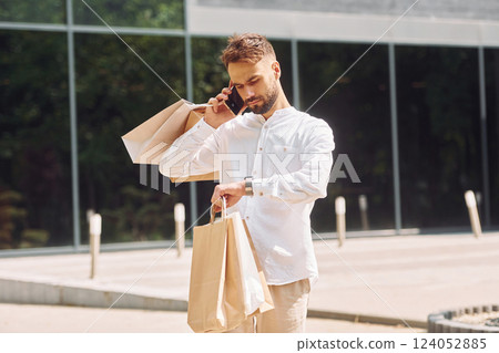 Against building with big windows. Stylish young man have shopping day. Outdoors with bags 124052885