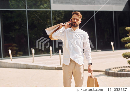 Standing near modern building. Stylish young man have shopping day. Outdoors with bags 124052887