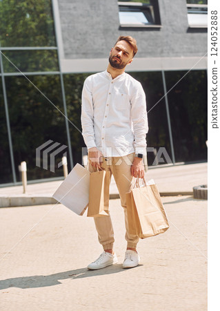 Standing near modern building. Stylish young man have shopping day. Outdoors with bags 124052888