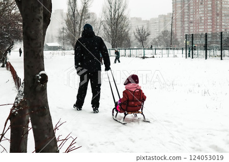 A father pulls sled with a child on a frosty cold winter day. A walk with a little kid in wintry season. Falling snowflakes in urban scene. Family fun A father pulls sled with a child on a frosty cold winter day. A walk with a little kid in wintry season. Falling snowflakes in urban scene. Family fun 124053019