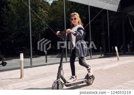 Little girl riding scooter outdoors near building outdoors 124053219