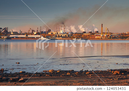 Industrial landscape. Port and factory on the river bank in bright sunset light. Smoke is coming from the pipes 124053431