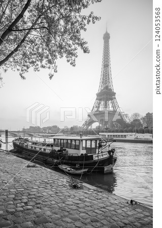 Dawn breaks over Paris as the Eiffel Tower stands tall, reflected in the calm Seine River. A boat is moored nearby, creating a tranquil atmosphere in the heart of the city. 124053568