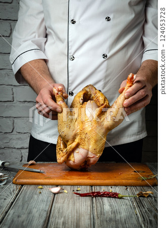 A skilled chef holds a whole chicken upside down, ready for preparation. The rustic wooden surface and textured wall add character to the culinary atmosphere, highlighting the art of cooking 124053728