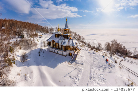 Aerial top view to wooden church of Transfiguration covered snow of the Lord on mountain near village Port Baikal. Frozen ice Lake and river Angara on backgroud. Winter landscape Siberia, Russia. Aerial top view to wooden church of Transfiguration covered snow of the Lord on mountain near village Port Baikal. Frozen ice Lake and river Angara on backgroud. Winter landscape Siberia, Russia. 124055677