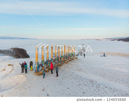 Aerial top view of famous Cape Burhan. Tourists tie colorful ribbons to wooden ritual poles and make wishes. Frozen Baikal Lake. Shaman rock and small sea. Clear ice, Khuzhir village, Olkhon, Russia 124055680
