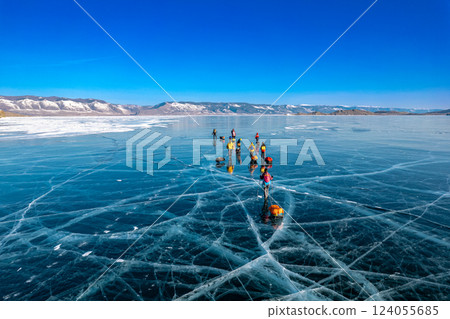 Aerial top view to tourist walk go on smooth surface. People with sleds moves along the blue clear ice. Winter crossing of Lake Baikal. Cracks glossy hummocks snow. Olkhon, Small Sea, Siberia, Russia Aerial top view to tourist walk go on smooth surface. People with sleds moves along the blue clear ice. Winter crossing of Lake Baikal. Cracks glossy hummocks snow. Olkhon, Small Sea, Siberia, Russia 124055685
