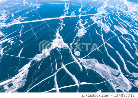 Aerial top view to Blue clear ice lake Baikal. Crack covered snow on frozen water surface. Cold winter landscape with mountains, sunny day, Natural background. , Russia, Siberia. Aerial top view to Blue clear ice lake Baikal. Crack covered snow on frozen water surface. Cold winter landscape with mountains, sunny day, Natural background. , Russia, Siberia. 124055712