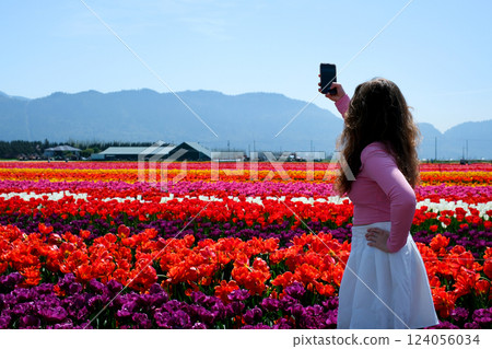 Portrait of a happy woman with hair flying in the wind against the backdrop of mountains and sea. Holding a bouquet of tulips Portrait of a happy woman with hair flying in the wind against the backdrop of mountains and sea. Holding a bouquet of tulips 124056034