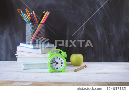 Back to school, stationery, alarm clock, stack of books, on wooden table with chalkboard background. 124057185