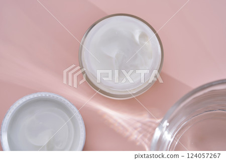 An open jar of cream with its texture on a pink background. 124057267