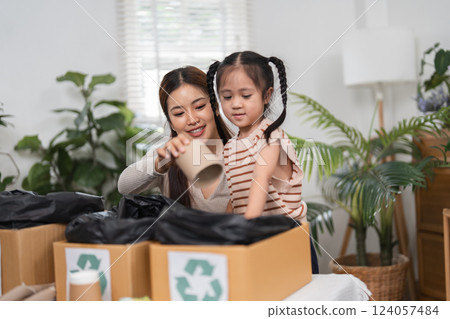 Waste Management and Family Interaction. A joyful mother and daughter practice recycling, sorting items to promote eco-friendly habits at home. 124057484