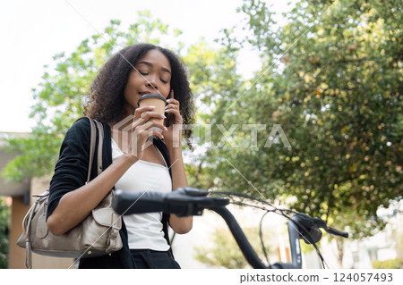 Sustainable Mobility and Well-Being. A woman enjoys her coffee while chatting on the phone beside her bicycle. 124057493