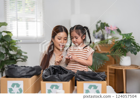 Hands-On Recycling and Family Values. A mother teaches her daughter about eco-friendly recycling at home. 124057504