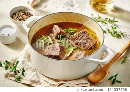 Hearty beef stew simmering in a white pot with fresh herbs and spices on a kitchen counter Hearty beef stew simmering in a white pot with fresh herbs and spices on a kitchen counter 124057798