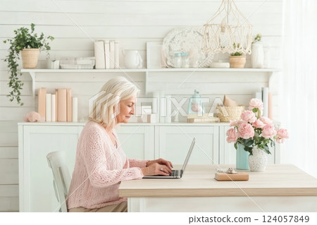 Elderly woman working on laptop at a cozy home office with floral decor and natural light Elderly woman working on laptop at a cozy home office with floral decor and natural light 124057849