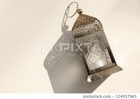 Golden metal ornamental Moroccan lantern on beige table in sunlight, long shadows. Flat lay, top view. Festive banner still life for Muslim holiday Ramadan Kareem. Eid mubarak celebration. 124057965