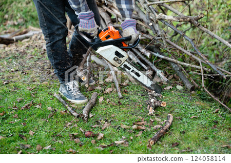 Using a chainsaw to cut branches in a backyard during early autumn, creating a space for new growth and landscaping 124058114