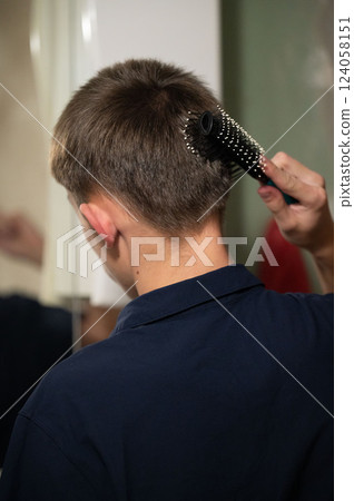 Young person styling their hair in front of a mirror, showcasing dedication to self-care and personal grooming in a cozy indoor setting during the afternoon 124058151