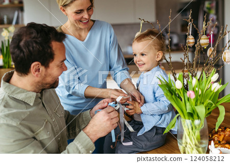 Parents helping little boy to decorate easter whip from willow branches with ribbons. Easter tradition concept. Parents helping little boy to decorate easter whip from willow branches with ribbons. Easter tradition concept. 124058212