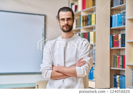 Portrait of young confident man with crossed arms posing inside library office Portrait of young confident man with crossed arms posing inside library office 124058820