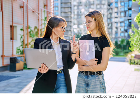 Female teacher talking to teenage student girl, outdoor, educational building background Female teacher talking to teenage student girl, outdoor, educational building background 124058822