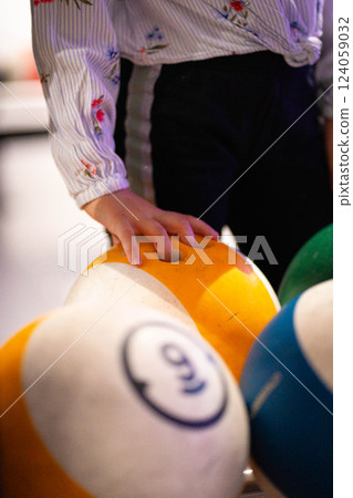 Hand reaching for vibrant bowling ball in colorful, well-lit bowling alley with various balls and blurred background creating dynamic atmosphere Hand reaching for vibrant bowling ball in colorful, well-lit bowling alley with various balls and blurred background creating dynamic atmosphere 124059032