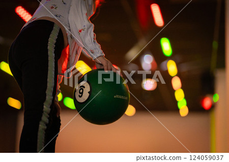 Hand reaching for vibrant bowling ball in colorful, well-lit bowling alley with various balls and blurred background creating dynamic atmosphere 124059037