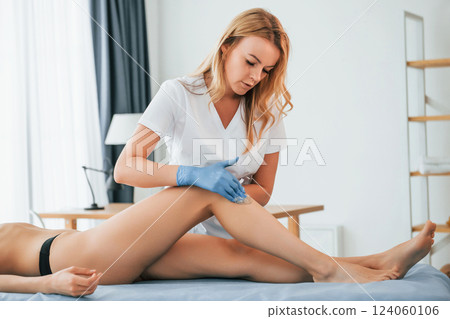 Putting cream on the legs. Woman is having sugaring procedure in the clinic by female doctor Putting cream on the legs. Woman is having sugaring procedure in the clinic by female doctor 124060106