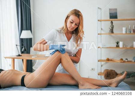 Putting cream on the legs. Woman is having sugaring procedure in the clinic by female doctor 124060108