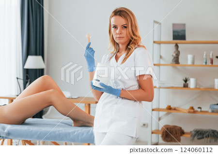 Holding stick with gel. Woman is having sugaring procedure in the clinic by female doctor Holding stick with gel. Woman is having sugaring procedure in the clinic by female doctor 124060112