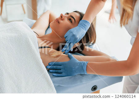 Putting cream on the armpits. Woman is having sugaring procedure in the clinic by female doctor Putting cream on the armpits. Woman is having sugaring procedure in the clinic by female doctor 124060114
