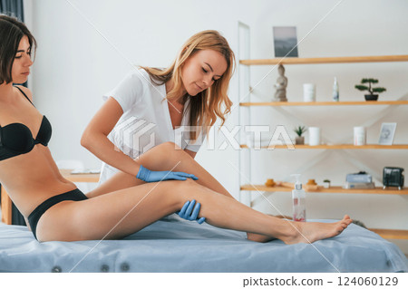 Putting cream on the legs. Woman is having sugaring procedure in the clinic by female doctor Putting cream on the legs. Woman is having sugaring procedure in the clinic by female doctor 124060129