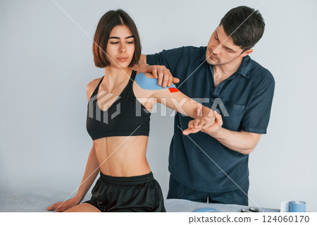 On the left hand. Woman visiting physiologist that putting kinesio tape on the skin On the left hand. Woman visiting physiologist that putting kinesio tape on the skin 124060170