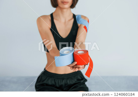 Female patient sitting in the clinic and holding kinesio tapes in hands Female patient sitting in the clinic and holding kinesio tapes in hands 124060184