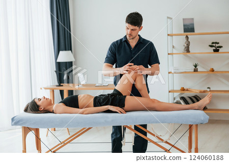 Moving the legs. Woman visiting physiologist that making massages and helping with traumas Moving the legs. Woman visiting physiologist that making massages and helping with traumas 124060188