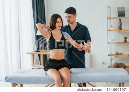 Modern background. Woman visiting physiologist that putting kinesio tape on the skin Modern background. Woman visiting physiologist that putting kinesio tape on the skin 124060197